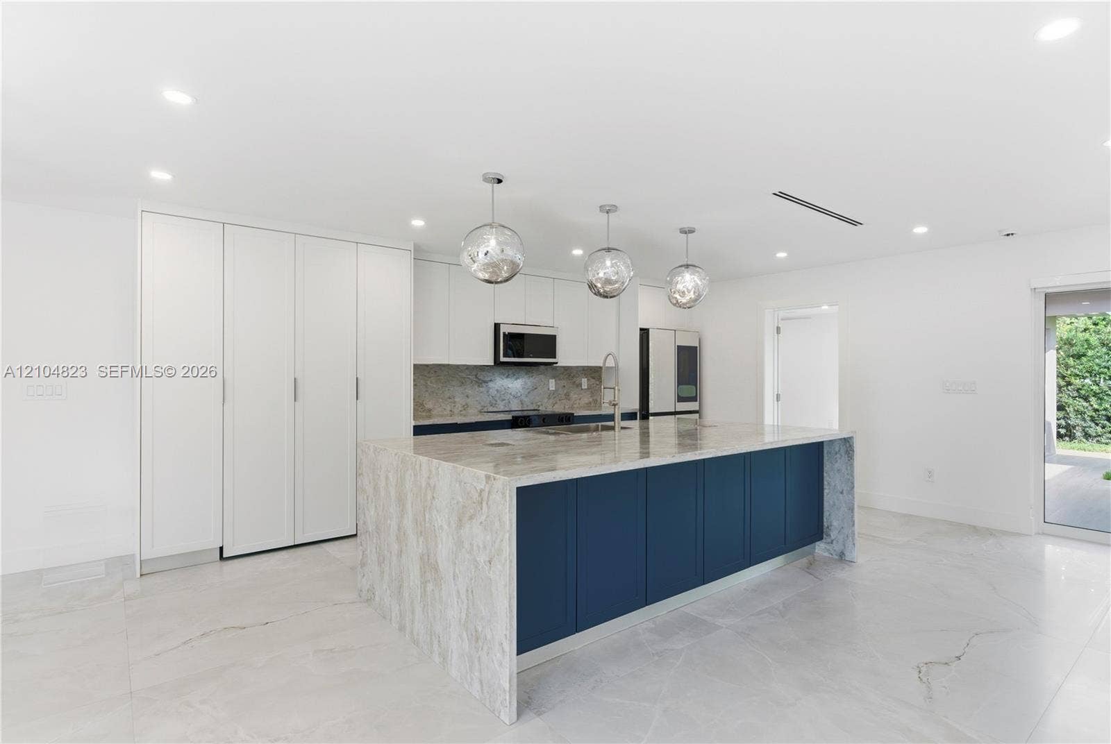 291 E Shore Drive E, Miami, FL 33133 Kitchen featuring floor-to-ceiling cabinetry, a central island with a waterfall countertop, stone backsplash, recessed lighting, and glass pendant fixtures