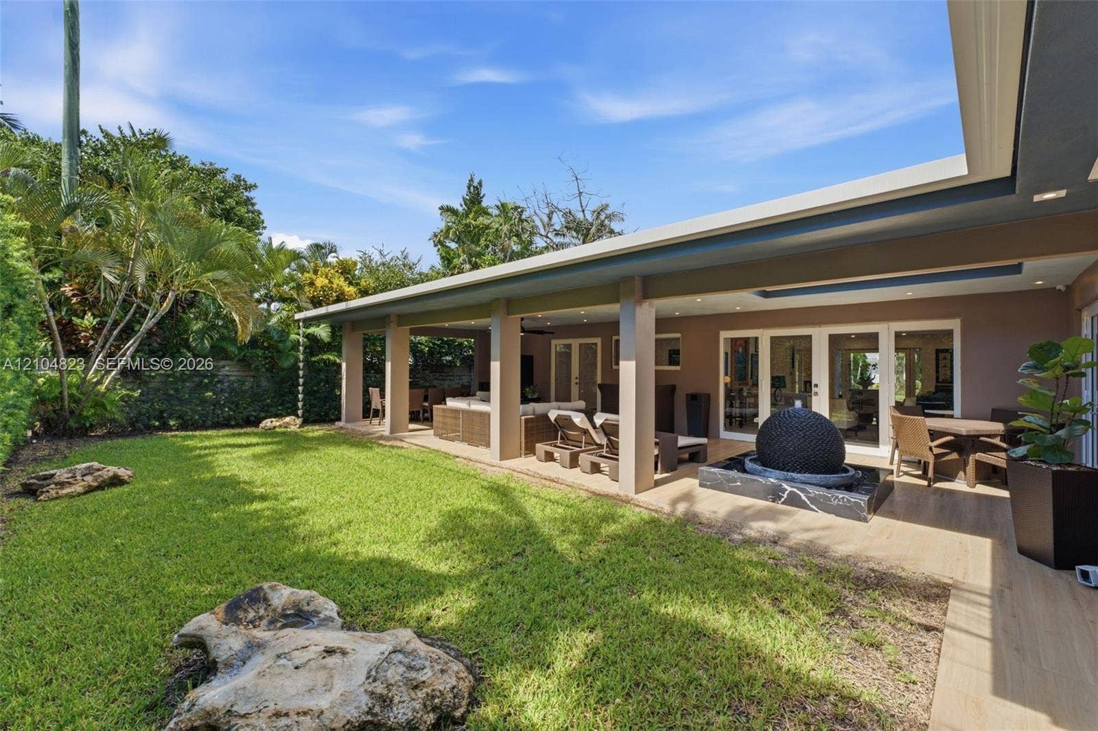 291 E Shore Drive E, Miami, FL 33133 Expansive green lawn with mature landscaping, covered patio with recessed lighting, and a modern water feature