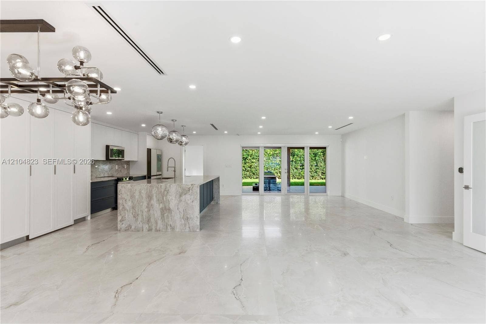 291 E Shore Drive E, Miami, FL 33133 Open-concept interior featuring large-format tile flooring, a stone-surround waterfall edge island, custom cabinetry, contemporary multi-globe light fixtures, and glass patio doors