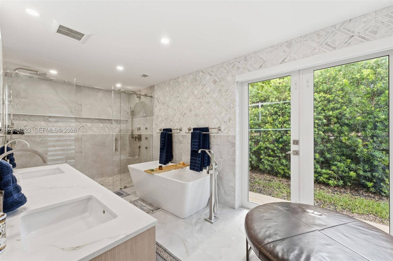 291 E Shore Drive E, Miami, FL 33133 Dual vanity with integrated sinks, freestanding soaking tub with floor-mounted faucet, glass-enclosed shower, wall-mounted towel bars, and French doors leading to exterior