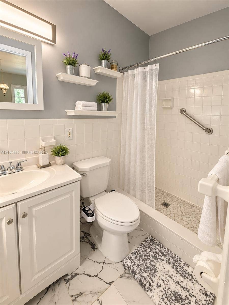 White tile wainscoting and bath surround, white vanity with integrated sink, floating wall shelving, white subway tile shower, and a pebble tile shower floor