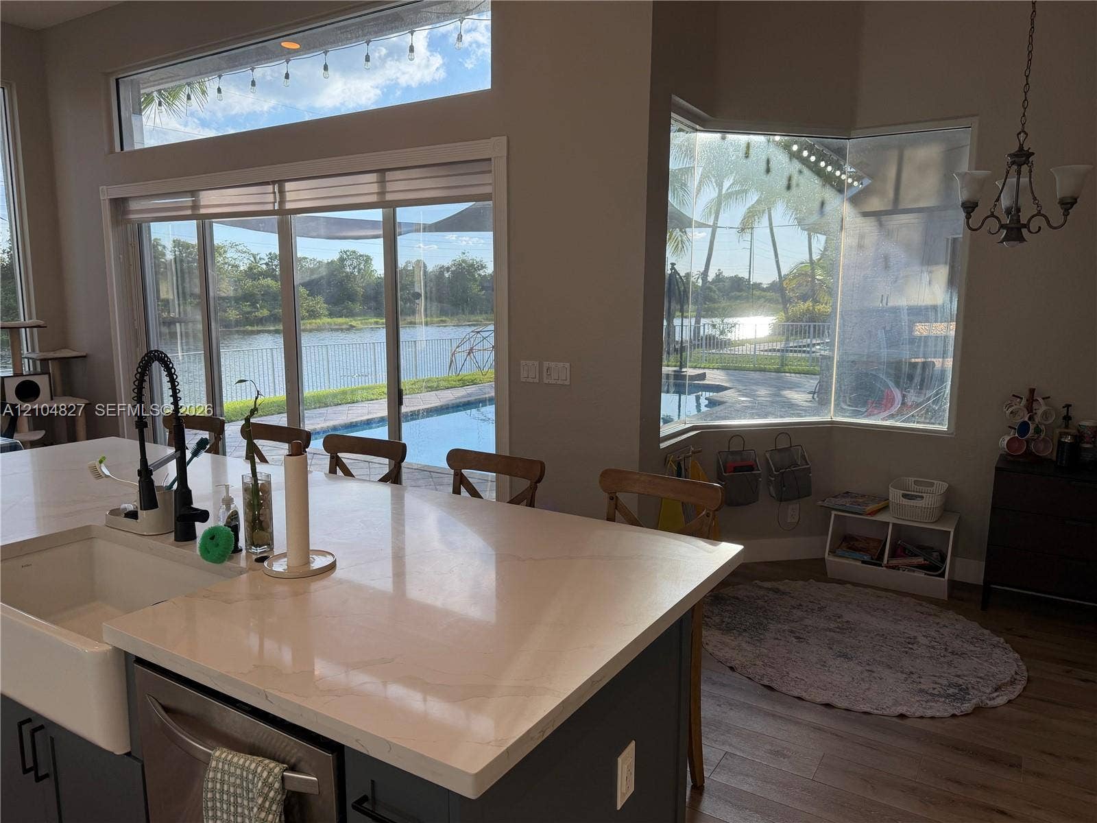 Kitchen featuring a large central island with quartz countertops, apron-front sink, and matte black faucet, complemented by wood-finish flooring, bay window, and sliding glass doors