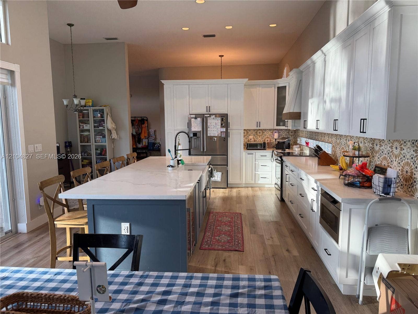 Kitchen featuring white shaker cabinetry, a contrasting navy blue center island with stone countertop, wood-finish flooring, patterned tile backsplash, and stainless steel appliances