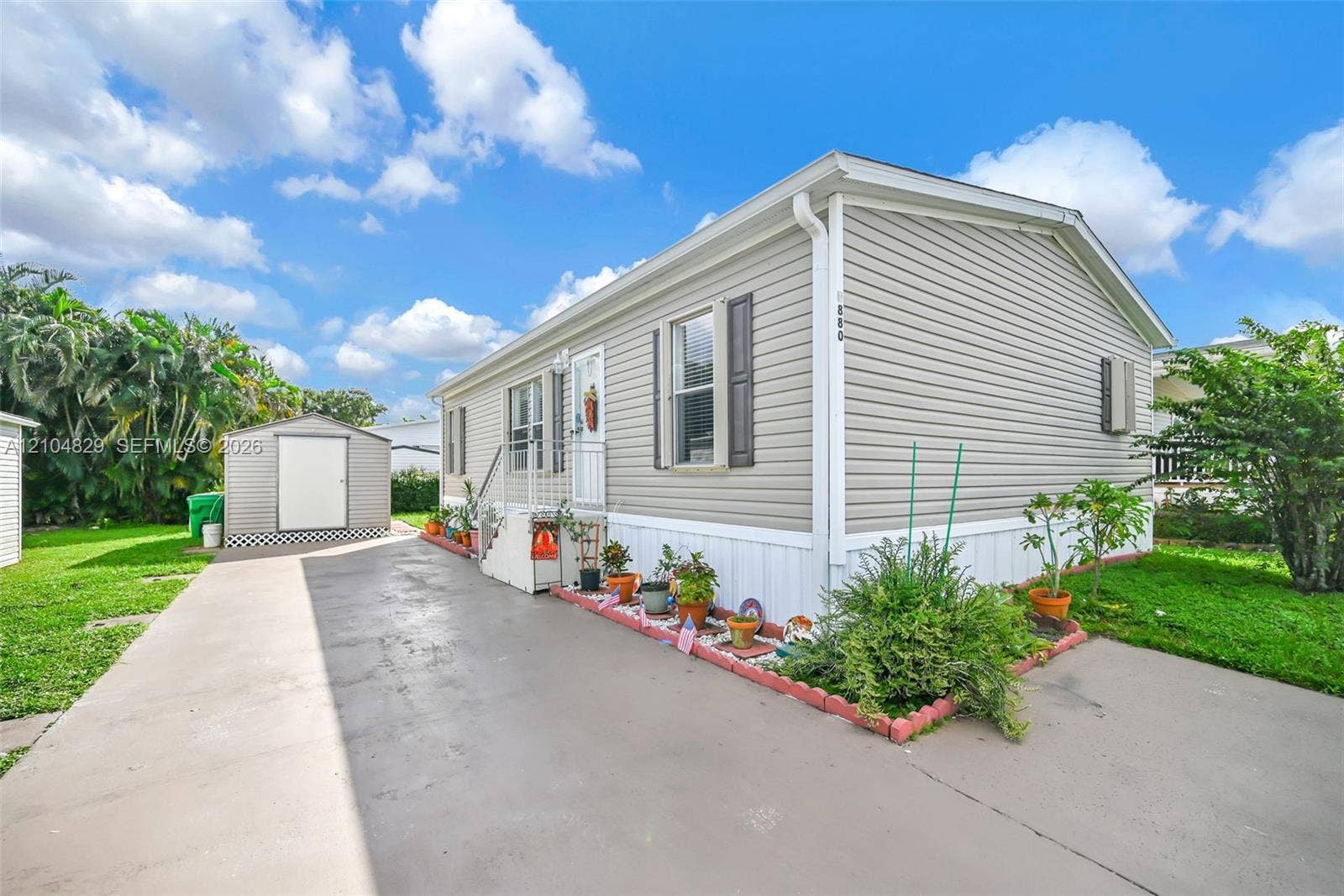 1880 SW 83rd Terrace, Davie, FL 33324 Exterior featuring light gray horizontal siding, an attached concrete driveway, a metal storage shed, and a concrete staircase leading to the entrance