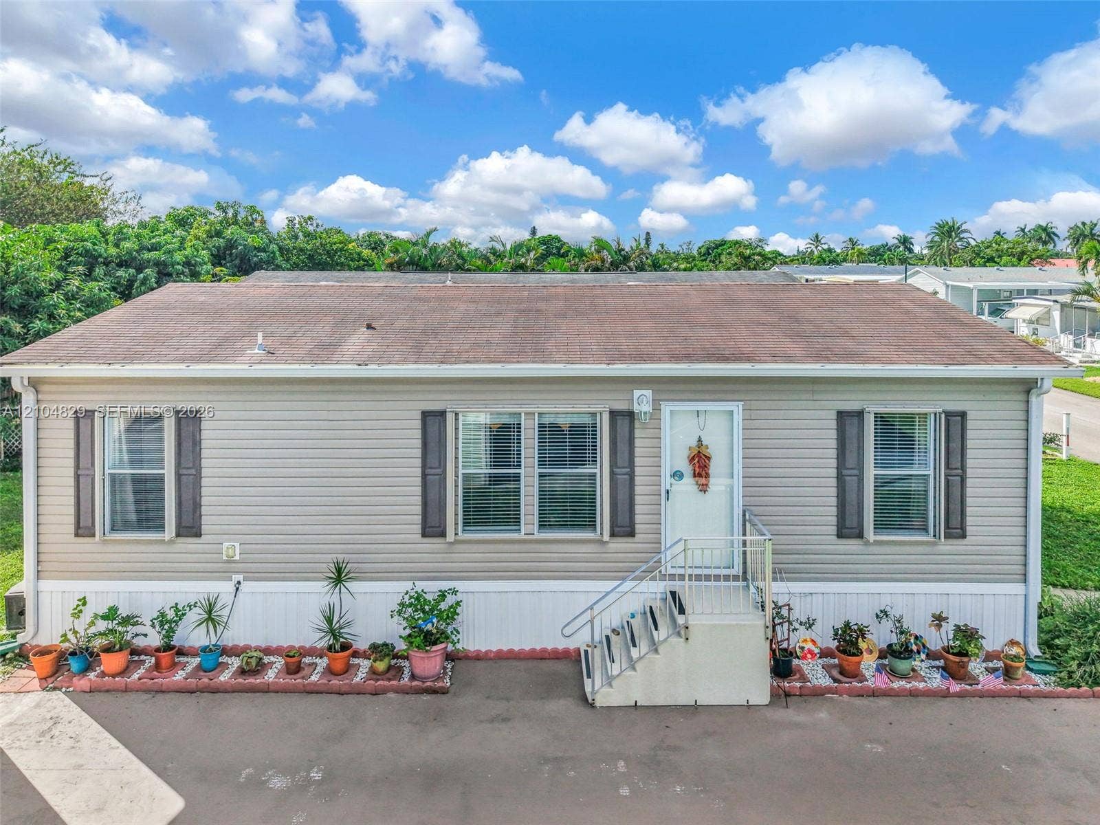 1880 SW 83rd Terrace, Davie, FL 33324 Single-story exterior featuring horizontal siding, dark louvered shutters, shingled roof, metal entry staircase with railings, and masonry-bordered landscape beds
