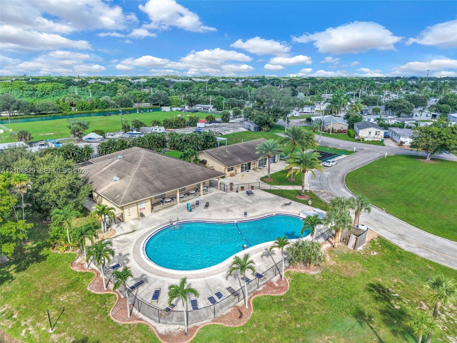 1880 SW 83rd Terrace, Davie, FL 33324 Community center featuring a kidney-shaped swimming pool, concrete pool deck, enclosed perimeter fencing, and established palm landscaping