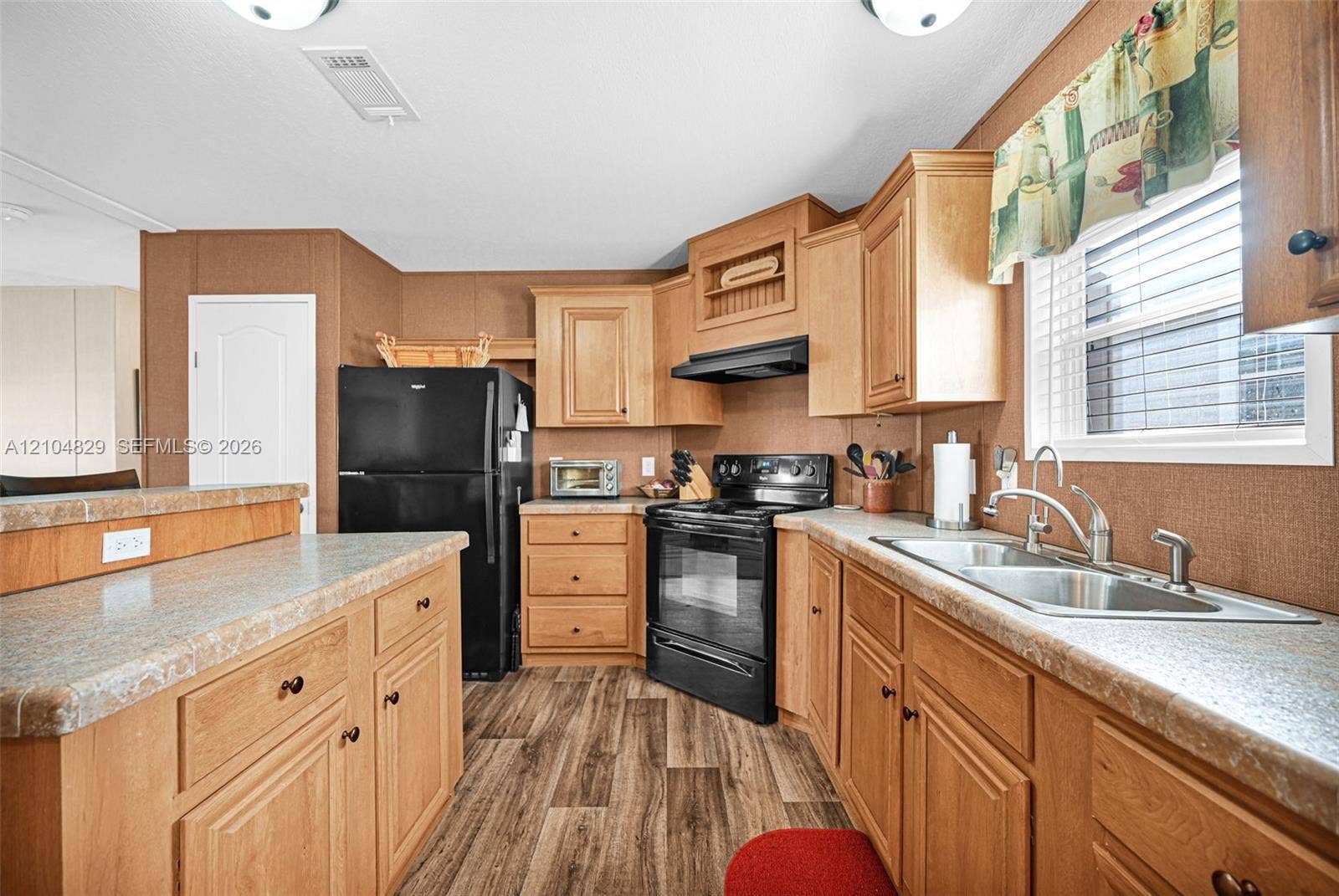 1880 SW 83rd Terrace, Davie, FL 33324 Kitchen featuring wood cabinetry, laminate countertops, a double-basin stainless steel sink, wood-finish flooring, and black appliances