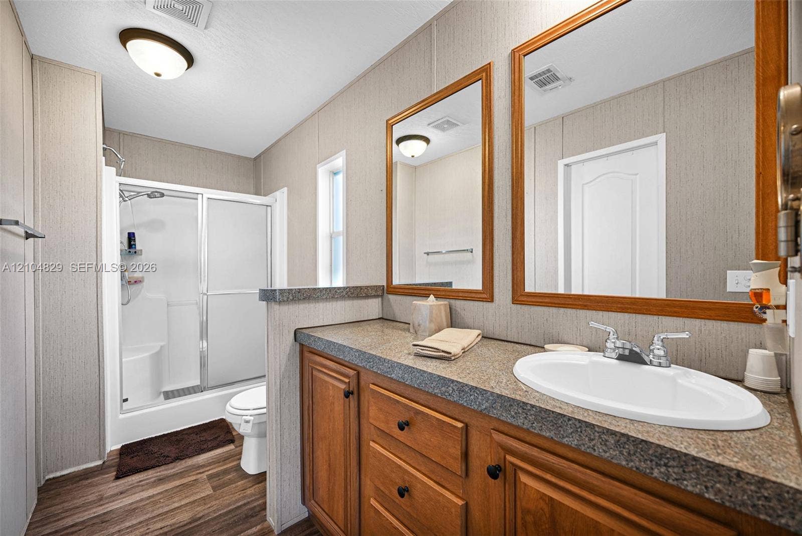 1880 SW 83rd Terrace, Davie, FL 33324 Bathroom featuring a wood-tone vanity with a dual-basin countertop, two framed mirrors, wood-finish flooring, and a walk-in shower enclosure