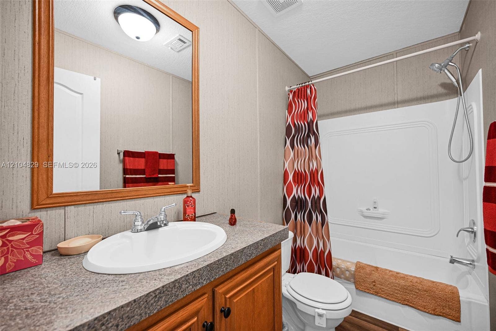 1880 SW 83rd Terrace, Davie, FL 33324 Bathroom featuring a wooden vanity, a stone-finish countertop with an inset oval sink, a large wood-framed mirror, and a tub-shower combination
