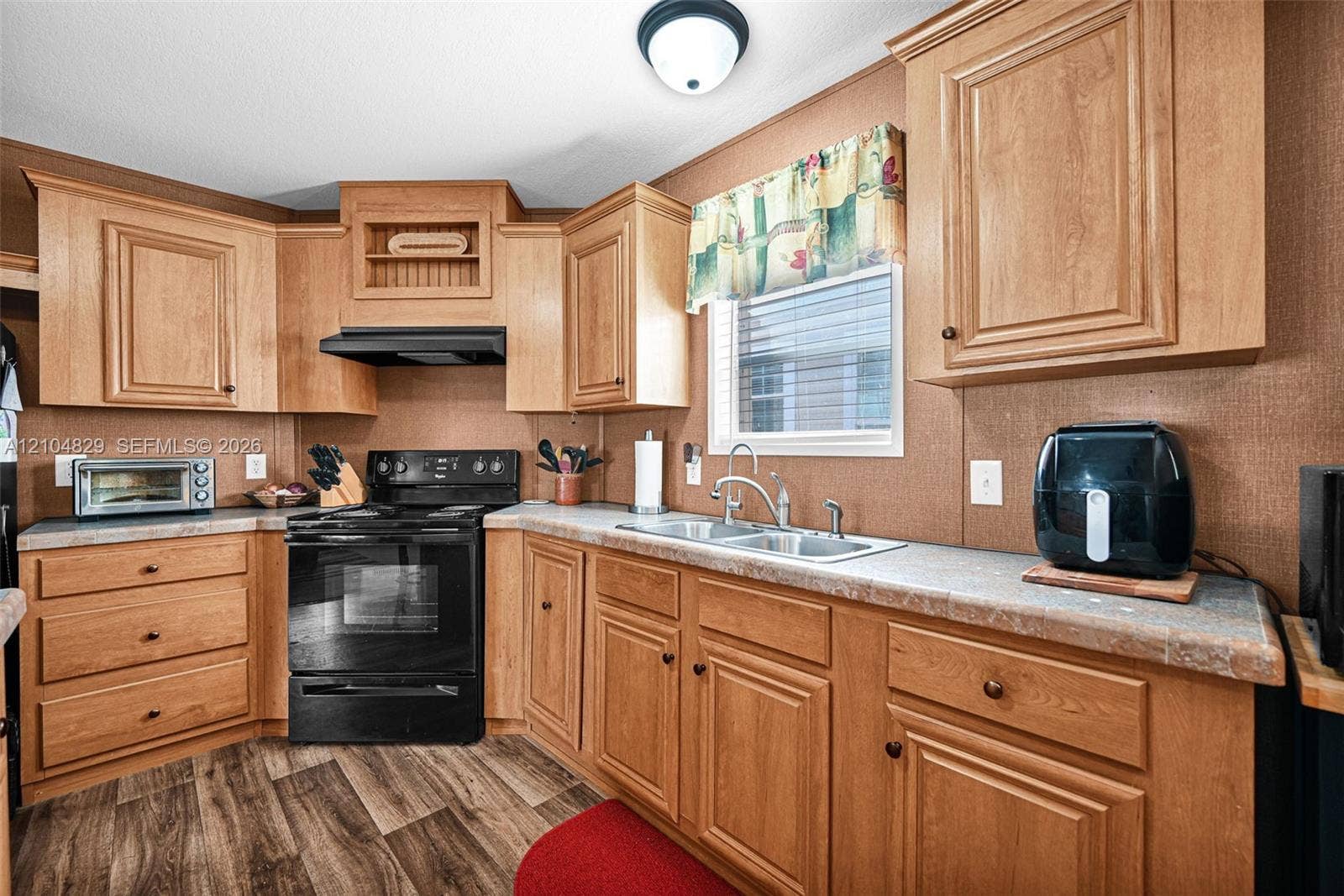 1880 SW 83rd Terrace, Davie, FL 33324 Kitchen featuring wood cabinetry, laminate countertops, integrated range hood, double-basin sink with faucet, and wood-finish flooring