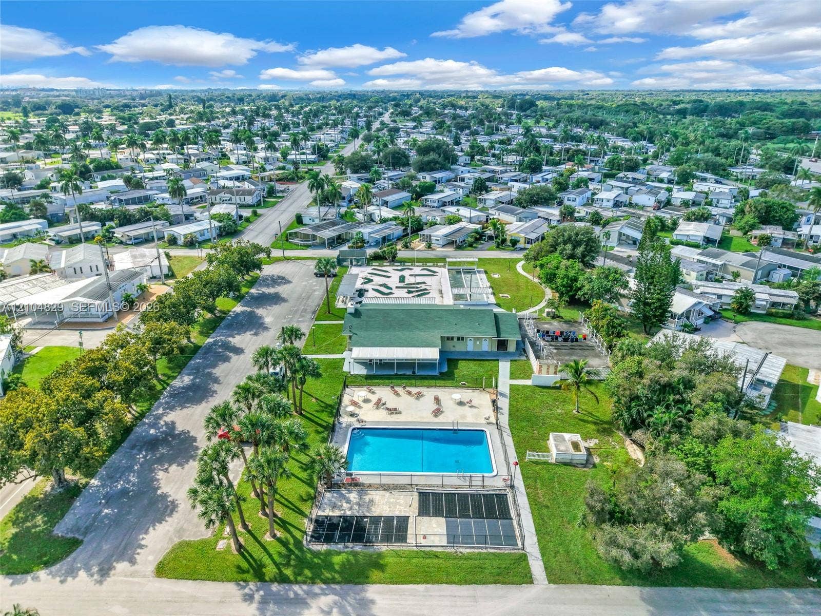 1880 SW 83rd Terrace, Davie, FL 33324 Aerial perspective featuring an outdoor swimming pool, paved pool deck, recreational hardscaping, mature palm trees, and a green shingle-roof building