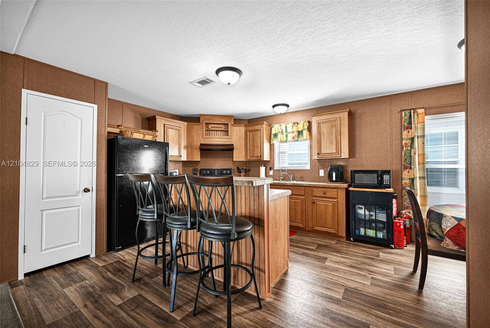 1880 SW 83rd Terrace, Davie, FL 33324 Kitchen featuring wood-finish cabinetry, a central breakfast bar, wood-finish flooring, dual flush-mount ceiling lighting, and a solid-panel door