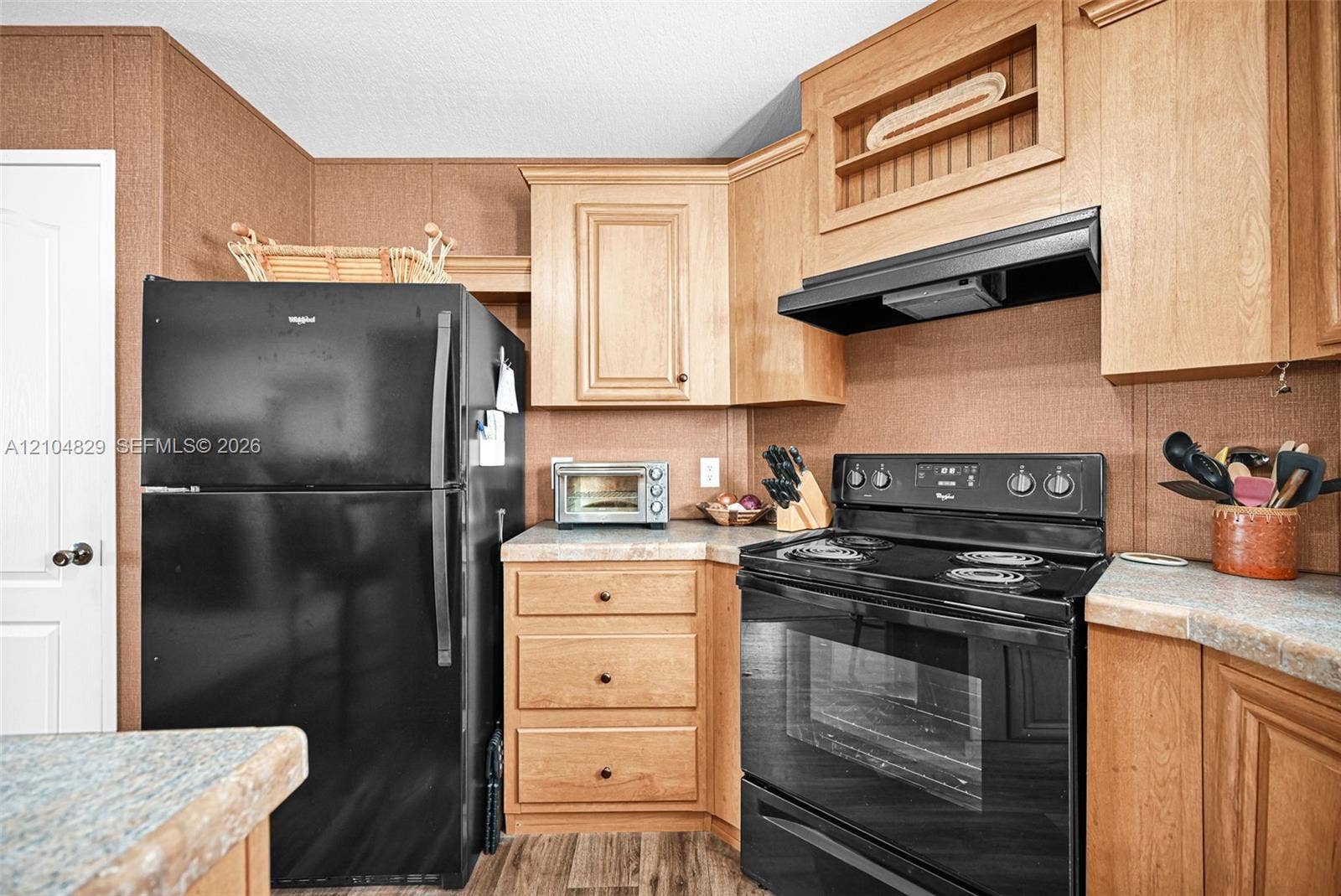1880 SW 83rd Terrace, Davie, FL 33324 Kitchen featuring light-tone wood cabinetry, black refrigerator, black range, integrated range hood, and solid-surface countertops