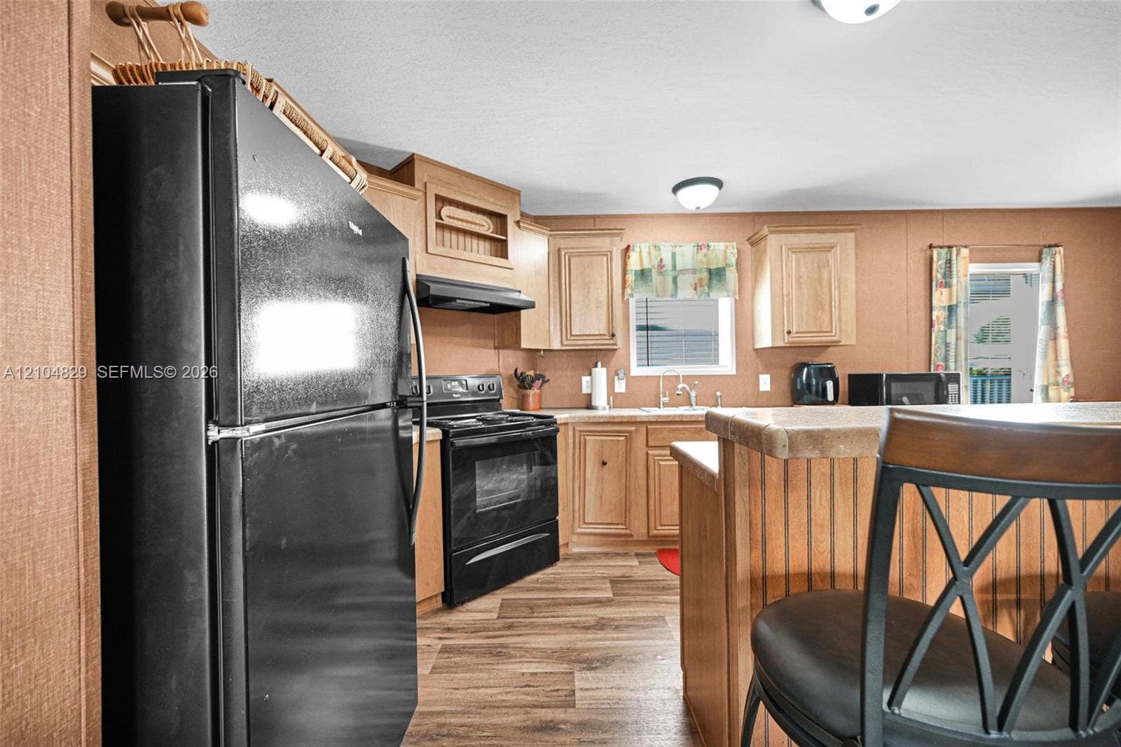 1880 SW 83rd Terrace, Davie, FL 33324 Kitchen featuring wood-finish cabinetry, black appliance package, wood-finish flooring, and a breakfast bar with a solid surface countertop