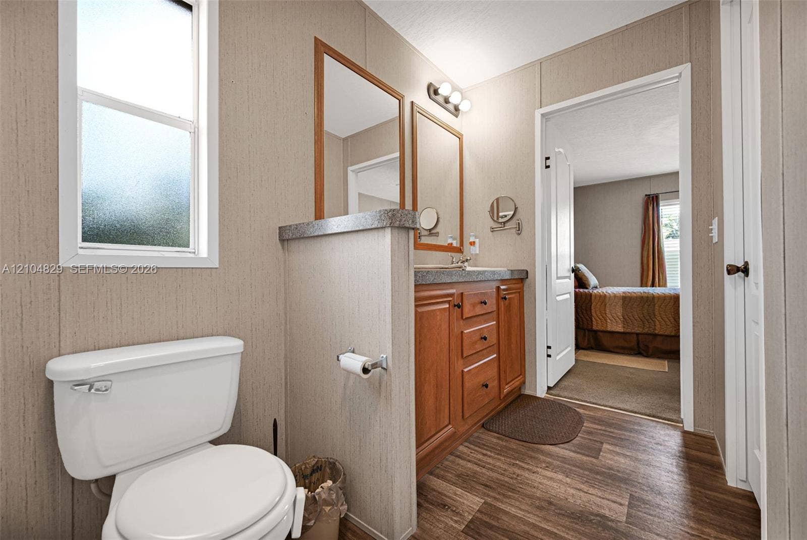 1880 SW 83rd Terrace, Davie, FL 33324 Bathroom featuring wood-finish flooring, a wood vanity with a stone-finish countertop, dual wall-mounted mirrors, and a frosted glass window