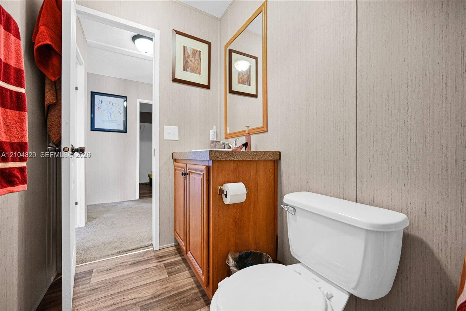 1880 SW 83rd Terrace, Davie, FL 33324 Bathroom featuring wood-finish cabinetry, a textured countertop, a wall-mounted mirror with a wood frame, and wood-finish flooring