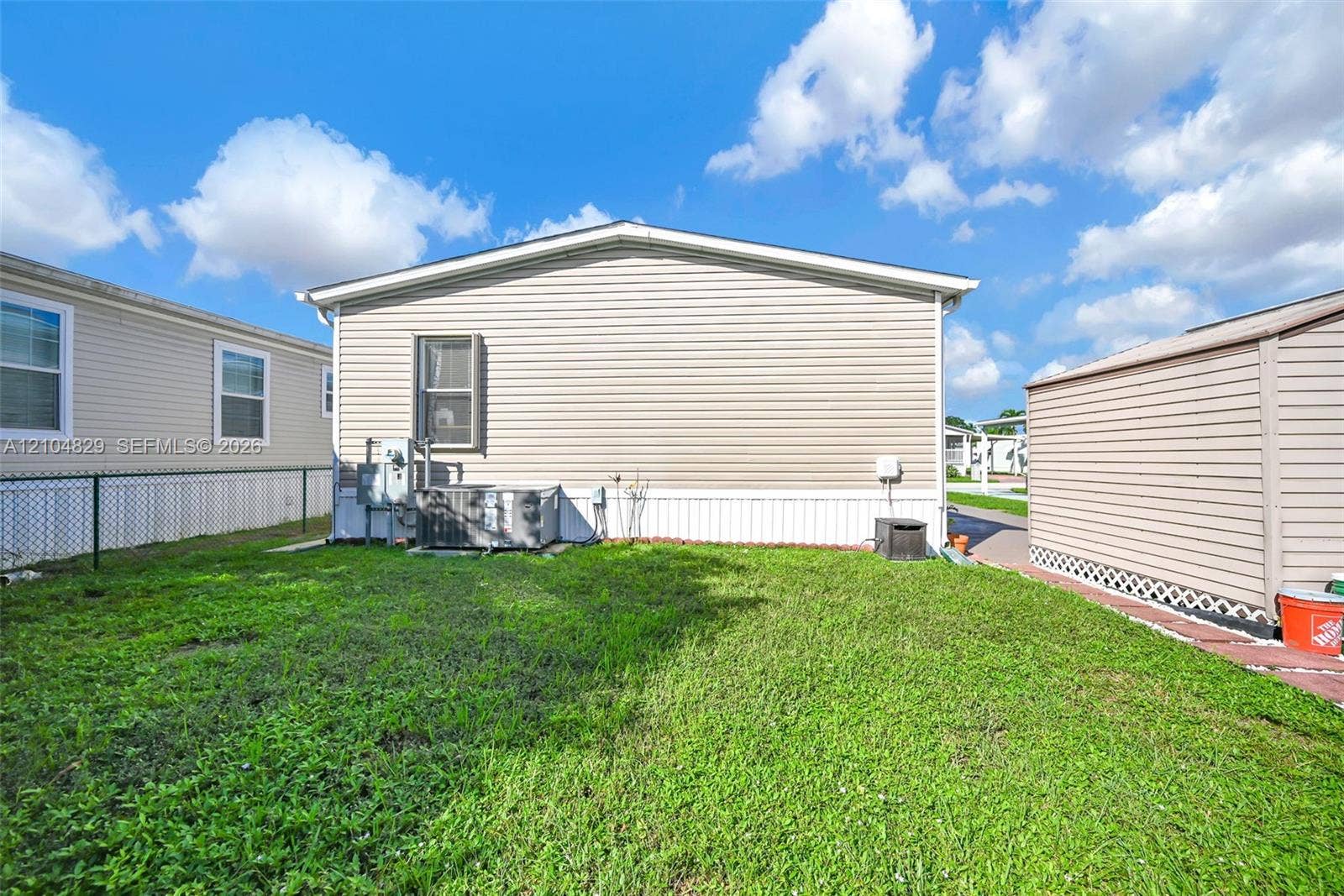 1880 SW 83rd Terrace, Davie, FL 33324 Exterior featuring light-toned horizontal siding, central air conditioning unit, chain-link fencing, and turf-covered yard area