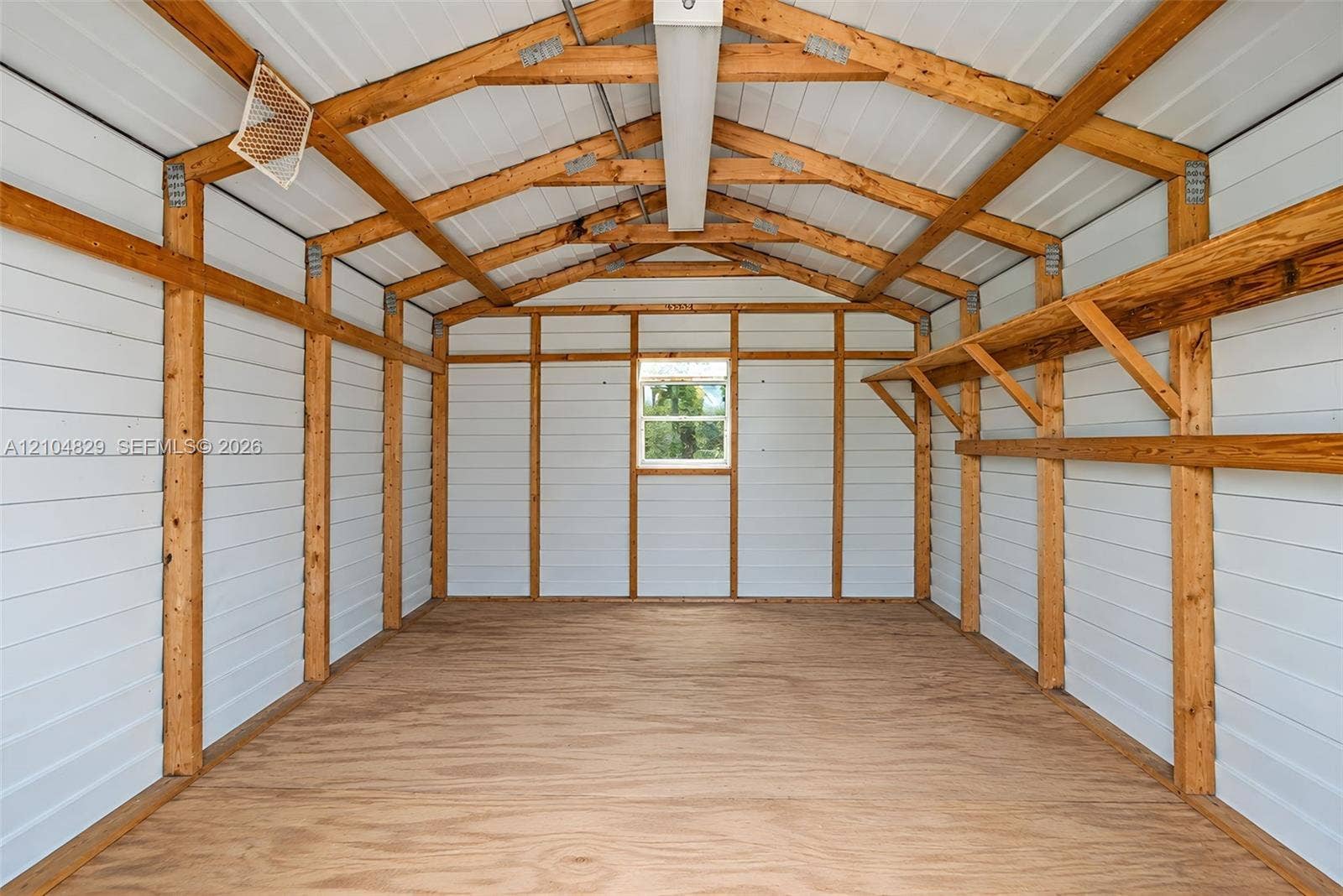 1880 SW 83rd Terrace, Davie, FL 33324 Exterior storage structure featuring exposed timber framing, white paneled walls, plywood flooring, integrated wall-mounted shelving, and a single window