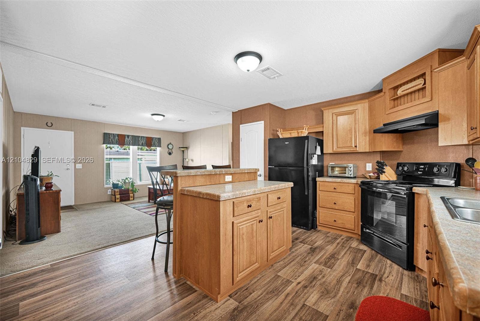1880 SW 83rd Terrace, Davie, FL 33324 Kitchen featuring wood-finish cabinetry, a central island with storage, stone-patterned countertops, and black appliance suite