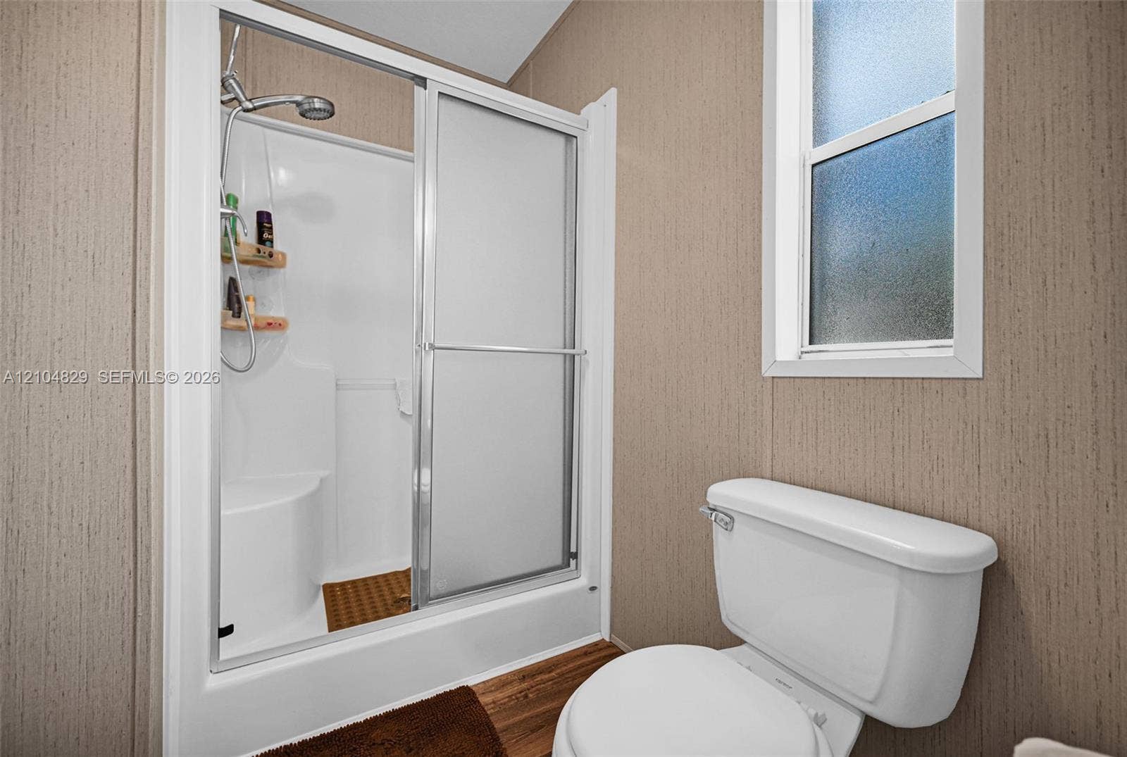 1880 SW 83rd Terrace, Davie, FL 33324 Walk-in shower enclosure featuring a built-in seat, adjustable shower head, and sliding glass doors, paired with a white porcelain toilet and vertical window with privacy glass