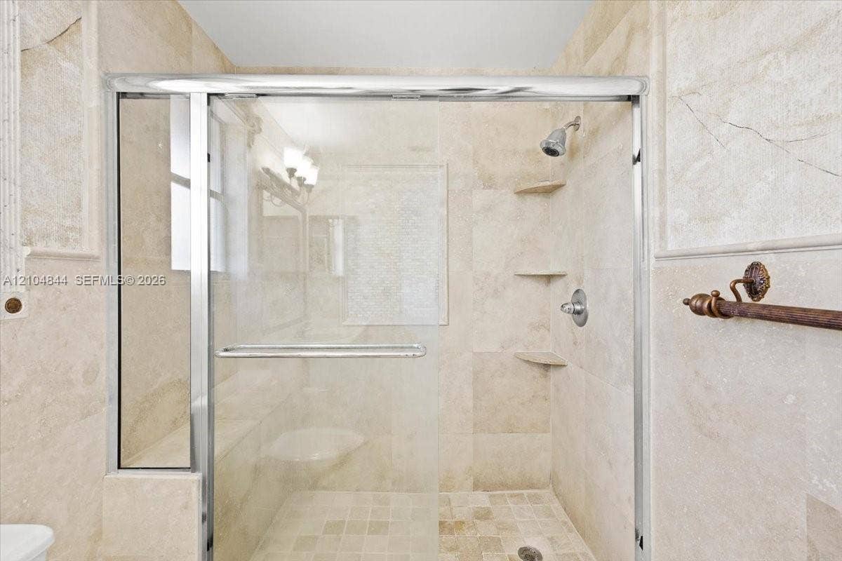 1216 NW 51st Way, Deerfield Beach, FL 33442 Walk-in shower featuring floor-to-ceiling stone tile, a glass enclosure with a polished metal frame, built-in stone shelving, and a wall-mounted shower head