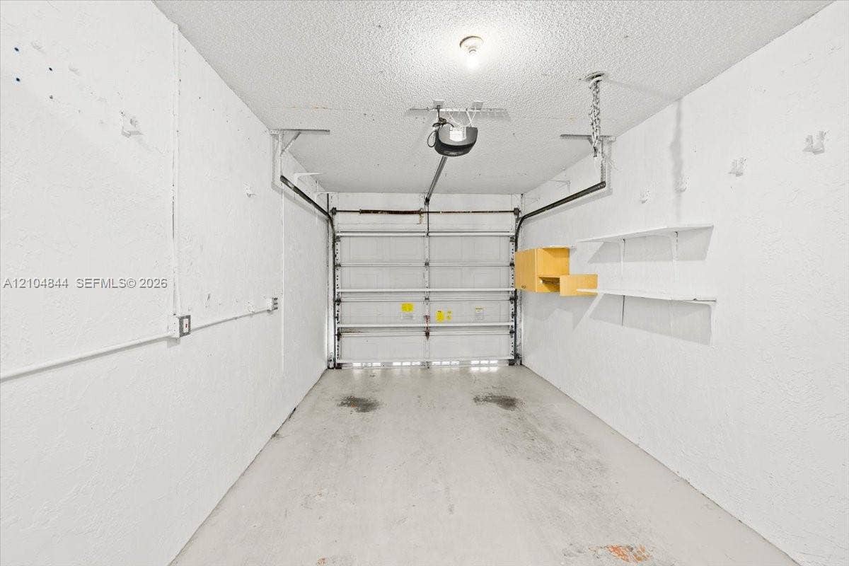 1216 NW 51st Way, Deerfield Beach, FL 33442 Single-car garage featuring a motorized door opener, concrete flooring, and built-in wall-mounted shelving