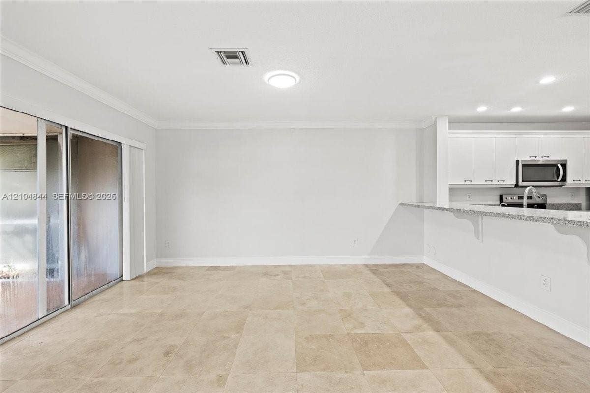 1216 NW 51st Way, Deerfield Beach, FL 33442 Open floor plan featuring large-format stone-finish flooring, white cabinetry, a breakfast bar with stone countertops, and sliding glass doors