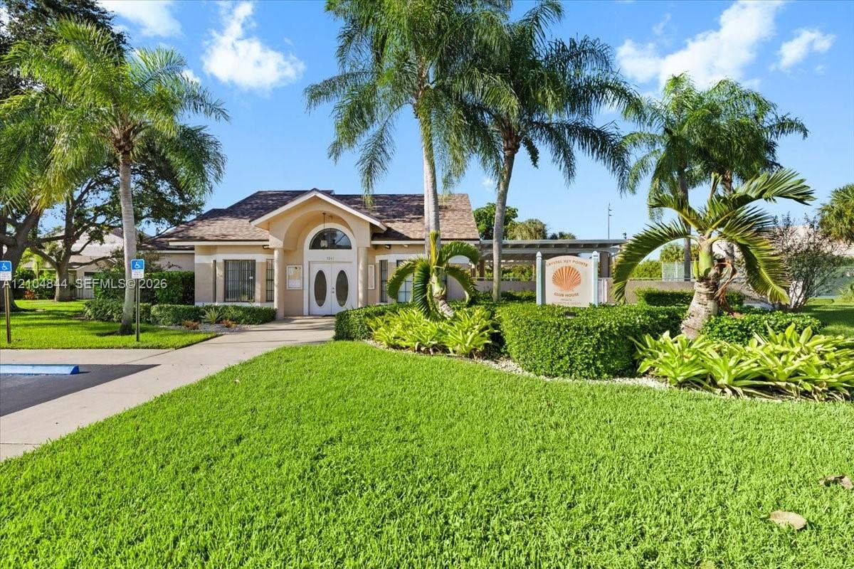 1216 NW 51st Way, Deerfield Beach, FL 33442 Stucco exterior with an arched entryway, double-door entrance, asphalt shingle roofing, manicured lawn, and mature palm trees