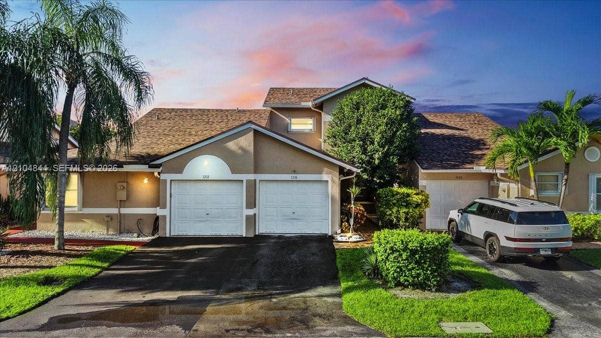 1216 NW 51st Way, Deerfield Beach, FL 33442 Stucco exterior featuring multiple garage bays, an asphalt driveway, and mature landscaping