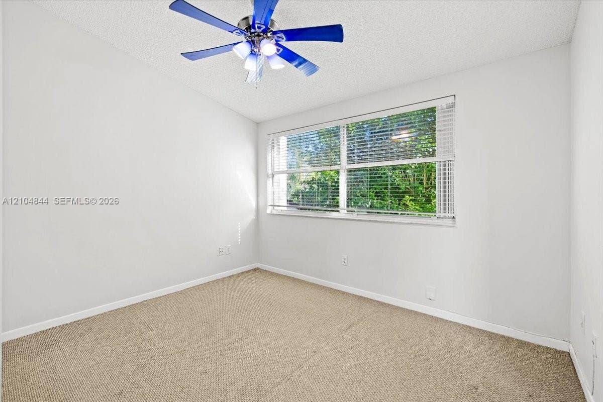1216 NW 51st Way, Deerfield Beach, FL 33442 Neutral wall tones, wall-to-wall carpeting, large horizontal window, and ceiling fan with integrated lighting