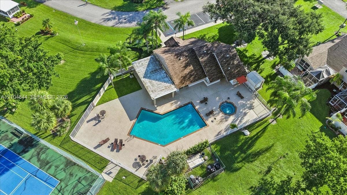 1216 NW 51st Way, Deerfield Beach, FL 33442 Aerial perspective of a property featuring an expansive paved patio, an in-ground swimming pool, a dedicated spa, a covered pergola, and a perimeter fence