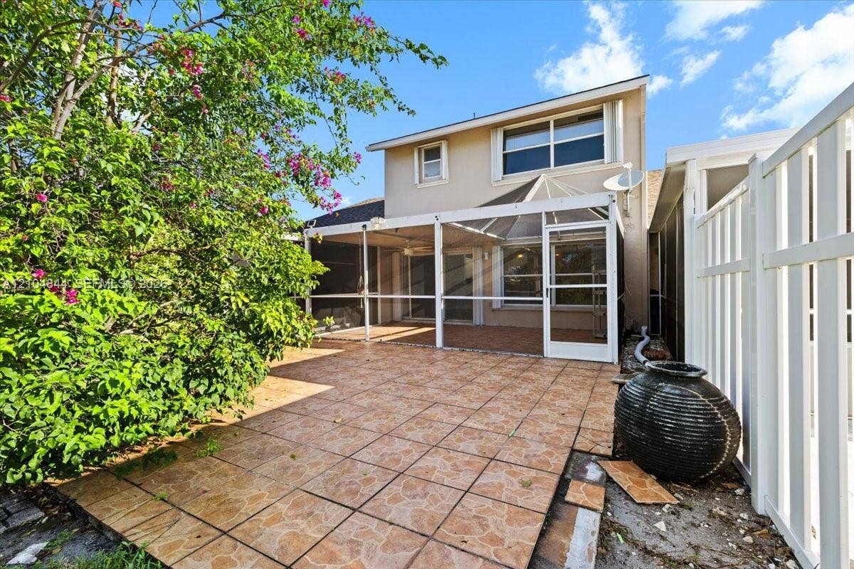 1216 NW 51st Way, Deerfield Beach, FL 33442 Rear exterior featuring a tiled patio and a covered, screen-enclosed porch area protected by a white vinyl privacy fence