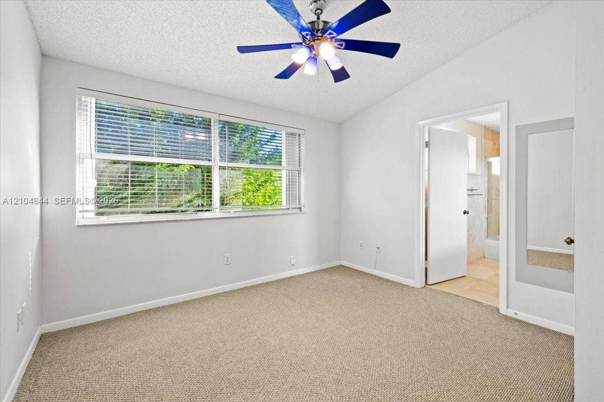1216 NW 51st Way, Deerfield Beach, FL 33442 Neutral-toned carpeting, multi-pane window with horizontal blinds, ceiling fan with integrated lighting, and inset wall-mounted mirror