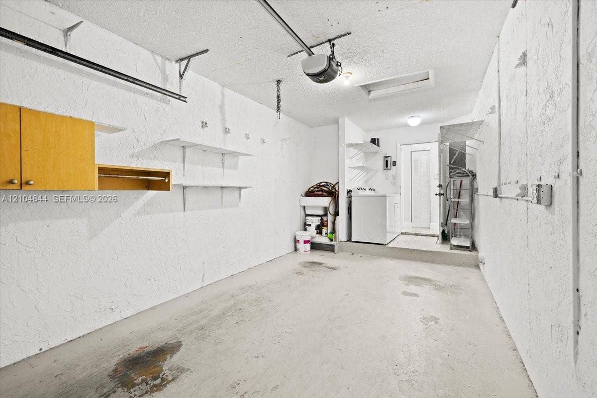 1216 NW 51st Way, Deerfield Beach, FL 33442 Garage featuring a concrete floor, built-in wooden wall cabinetry, fixed shelving units, utility sink, and a pedestrian door
