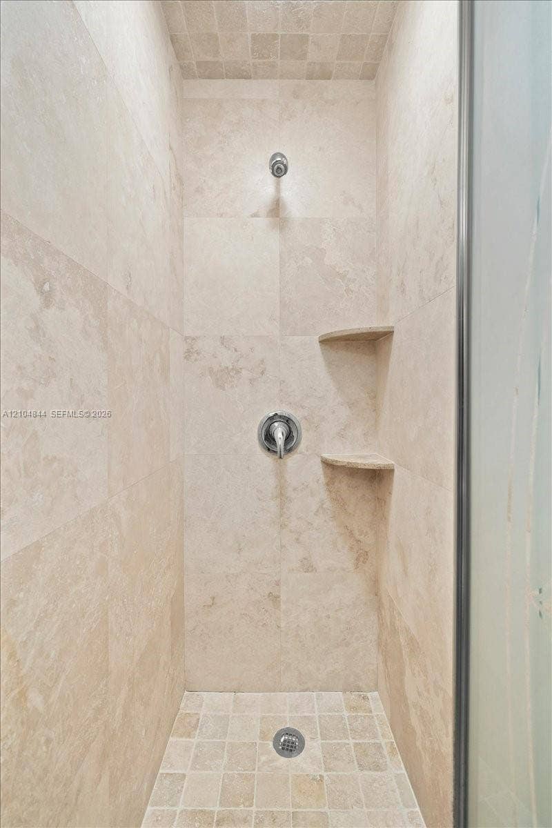 1216 NW 51st Way, Deerfield Beach, FL 33442 Shower stall featuring stone wall tiling, mosaic floor tile, built-in dual corner shelves, and a wall-mounted chrome fixture