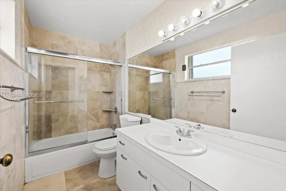 1216 NW 51st Way, Deerfield Beach, FL 33442 Bathroom featuring a white vanity with an integrated basin, a large wall-mounted mirror, a glass-enclosed shower and tub combination, and neutral-toned wall tiling