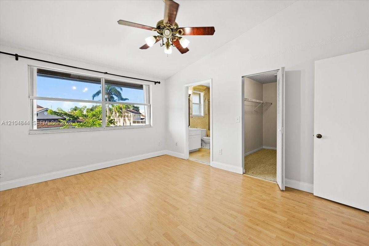 1216 NW 51st Way, Deerfield Beach, FL 33442 Bedroom featuring wood-finish flooring, vaulted ceiling, large multi-pane window, ceiling fan with light fixture, and closet with built-in shelving