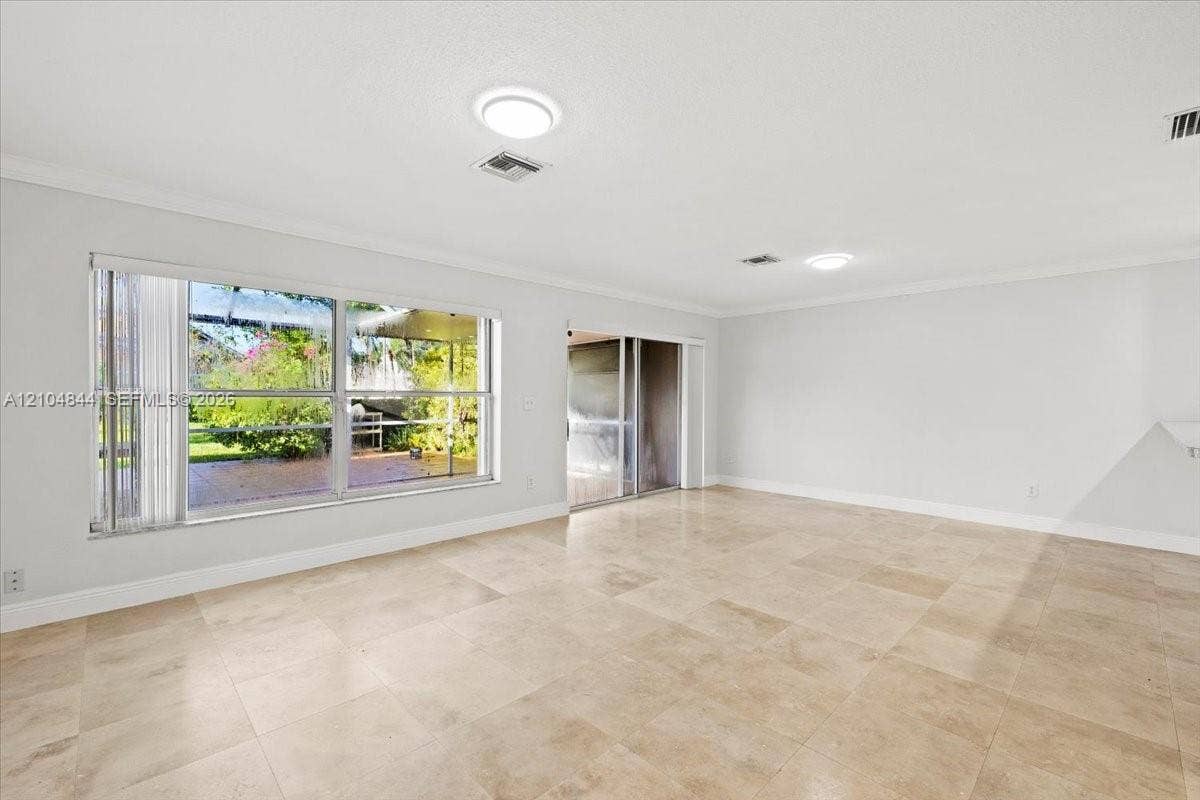 1216 NW 51st Way, Deerfield Beach, FL 33442 Spacious interior featuring large-format stone flooring, crown molding, expansive windows, and a sliding glass door providing natural light