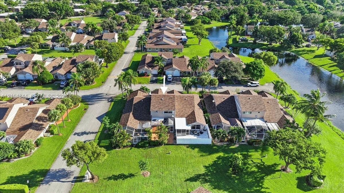 1216 NW 51st Way, Deerfield Beach, FL 33442 Multi-level townhome featuring a shingle roof, rear-facing screened-in patio, and direct access to expansive green space and water frontage