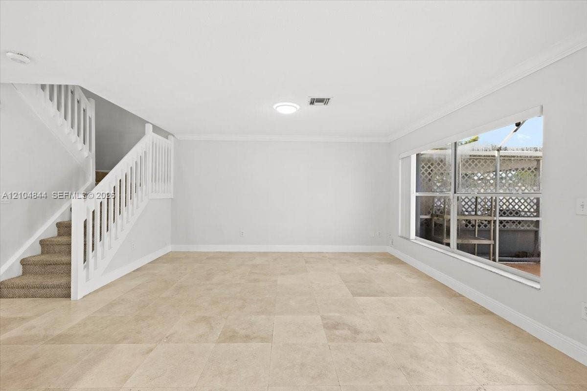 1216 NW 51st Way, Deerfield Beach, FL 33442 Open interior space featuring large-format stone-style tile flooring, white-painted walls, a staircase with a white wood balustrade, and a expansive window