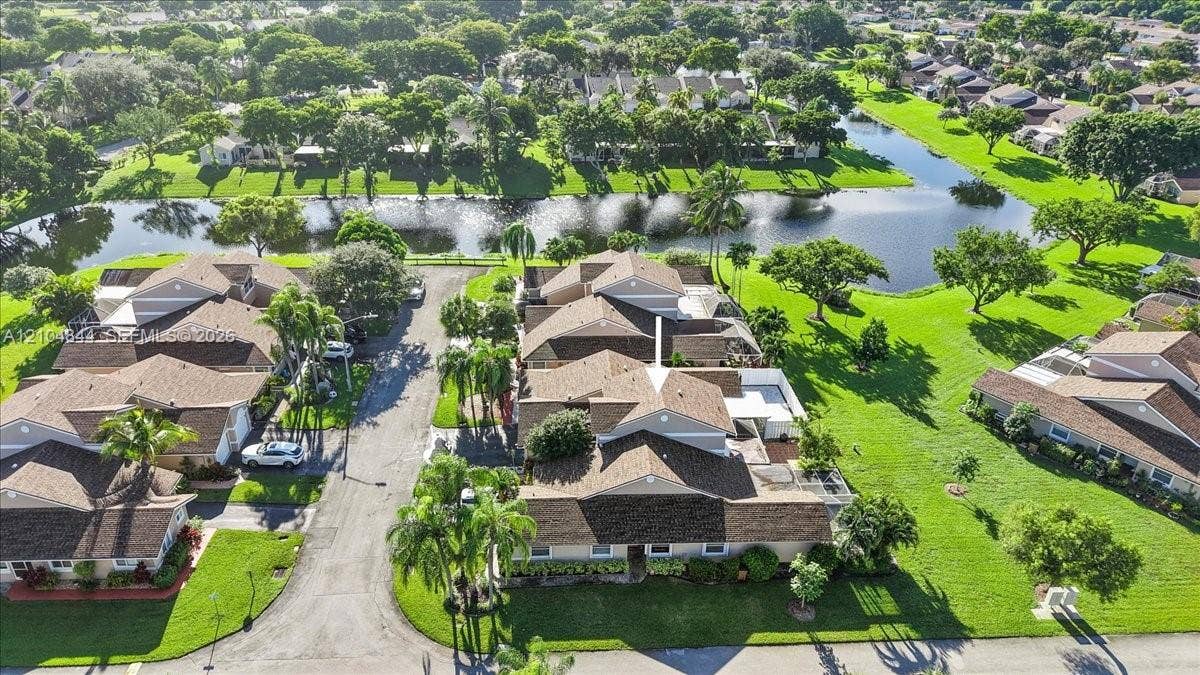 1216 NW 51st Way, Deerfield Beach, FL 33442 Aerial perspective of a multi-unit property featuring a shingle roof, paved access road, manicured lawn, and proximity to a water feature