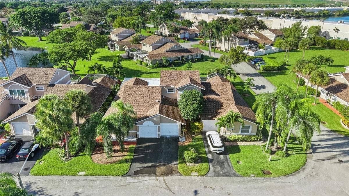 1216 NW 51st Way, Deerfield Beach, FL 33442 Aerial perspective of a multi-unit residential complex featuring gabled roofs, asphalt driveways, two-car garage doors, and established landscaping with mature palm trees