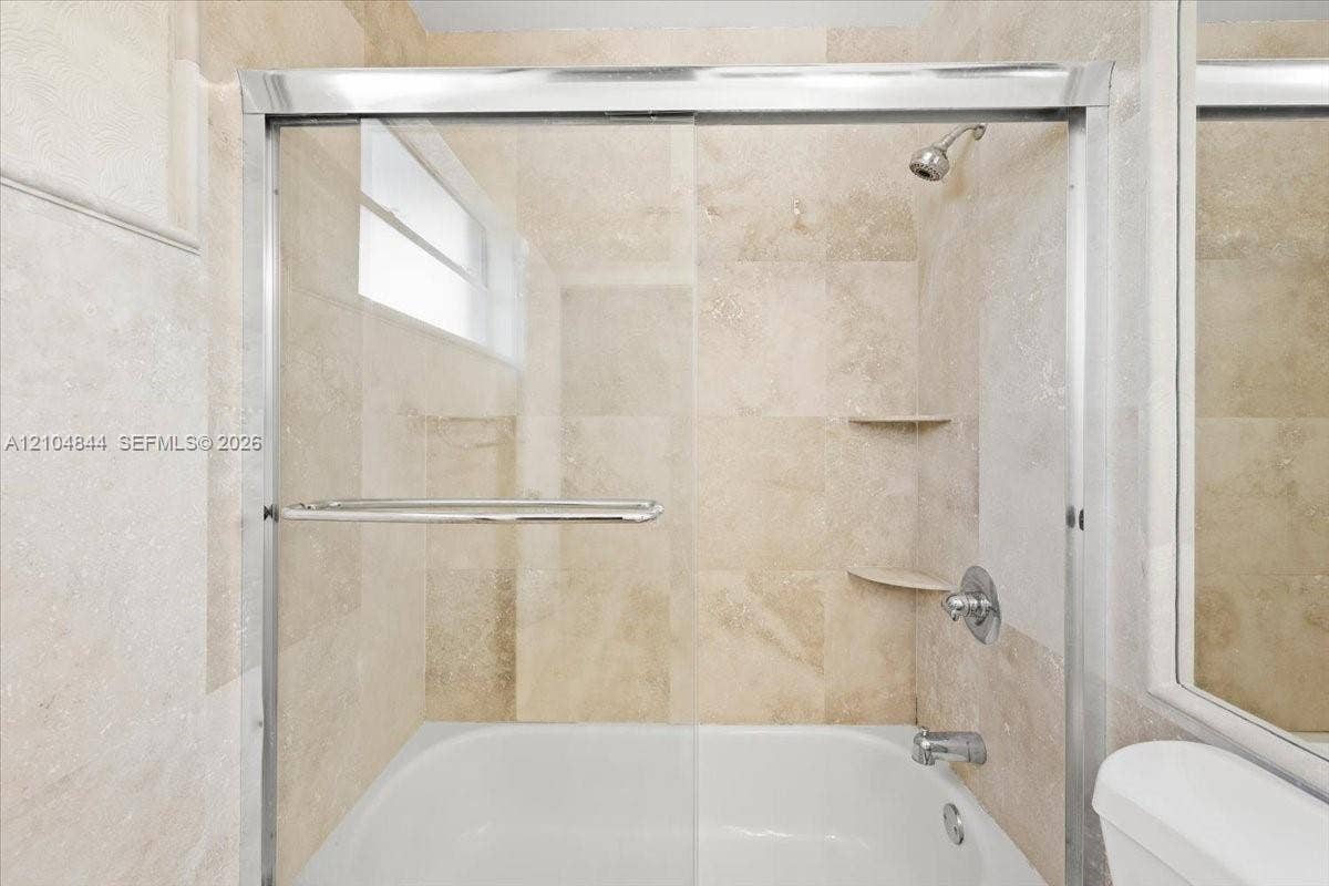 1216 NW 51st Way, Deerfield Beach, FL 33442 Full-height tiled shower surround featuring a sliding glass enclosure, integrated corner shelving, polished chrome fixtures, and a recessed window