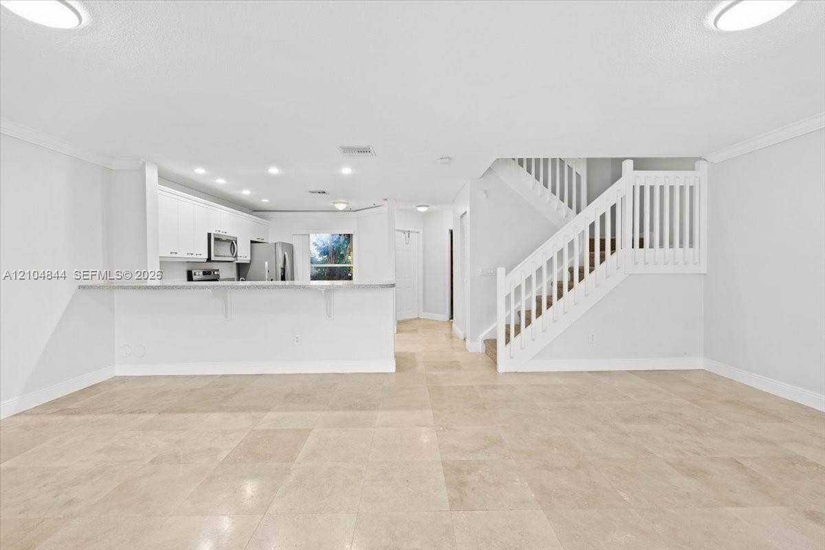 1216 NW 51st Way, Deerfield Beach, FL 33442 Open-concept interior featuring large-format tile flooring, white cabinetry, a breakfast bar with stone-finish countertops, recessed lighting, and a staircase with white balusters
