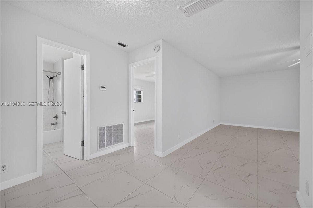 Large-format neutral-toned tile flooring with integrated veining, clean white wall finishes, and a bathroom featuring a shower-tub combination with white wall tile