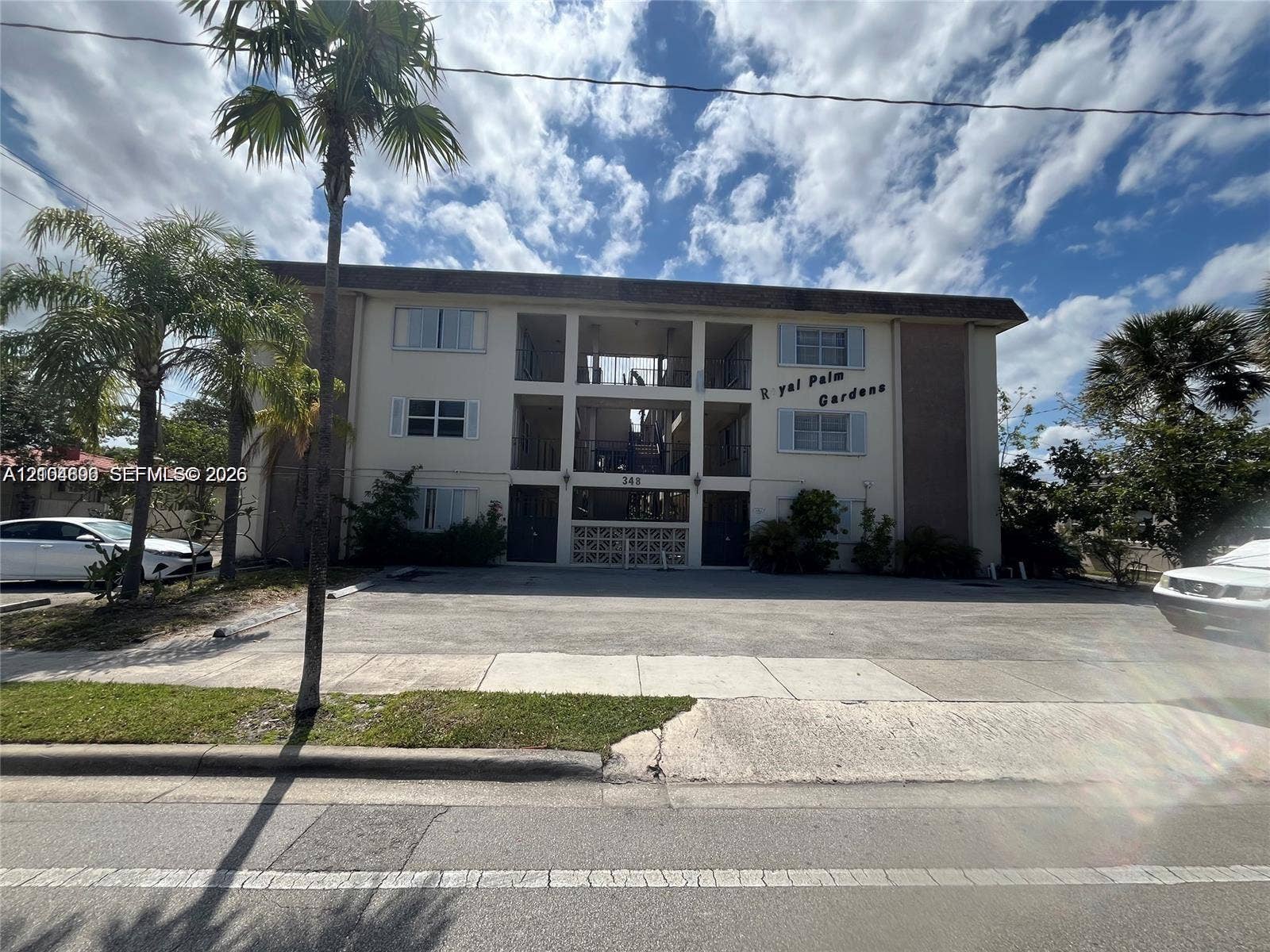 Three-story multi-unit structure featuring a concrete facade, decorative breezeblock accents, exterior stairwell, and surface parking