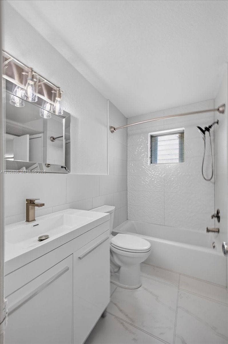 Bathroom featuring a white vanity with a rectangular sink, metallic faucet, wall-mounted mirror with integrated light fixture, and a white tile bathtub surround