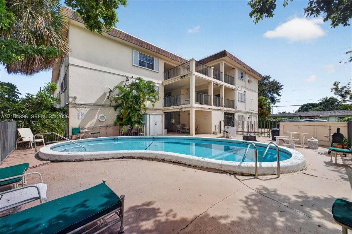 In-ground kidney-shaped swimming pool with a concrete deck, multi-level exterior balconies with metal railings, and stucco siding