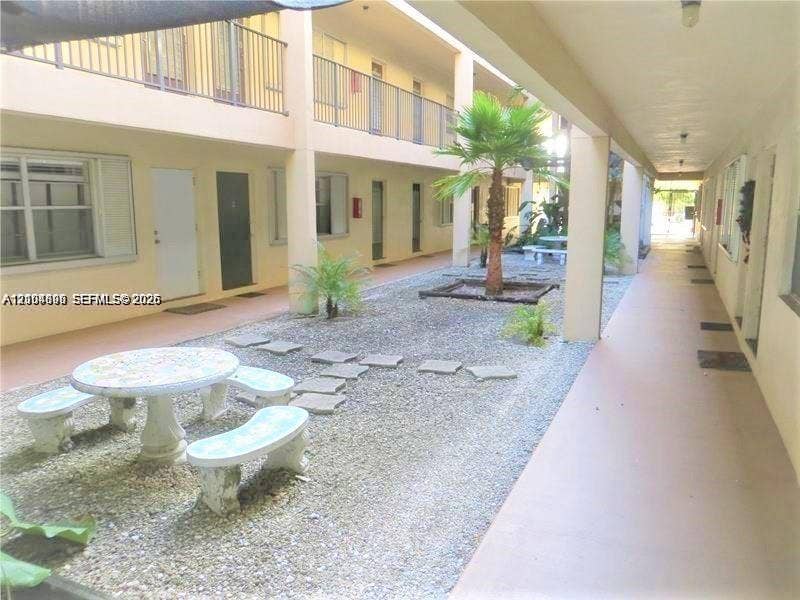 Open-air corridor featuring multiple levels, metal railings, gravel-based courtyard, and palm trees