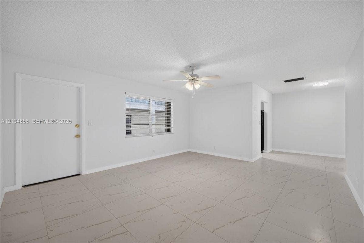 Interior space featuring light-toned tile flooring, neutral walls, a multi-blade ceiling fan with integrated lighting, and a window with horizontal blinds